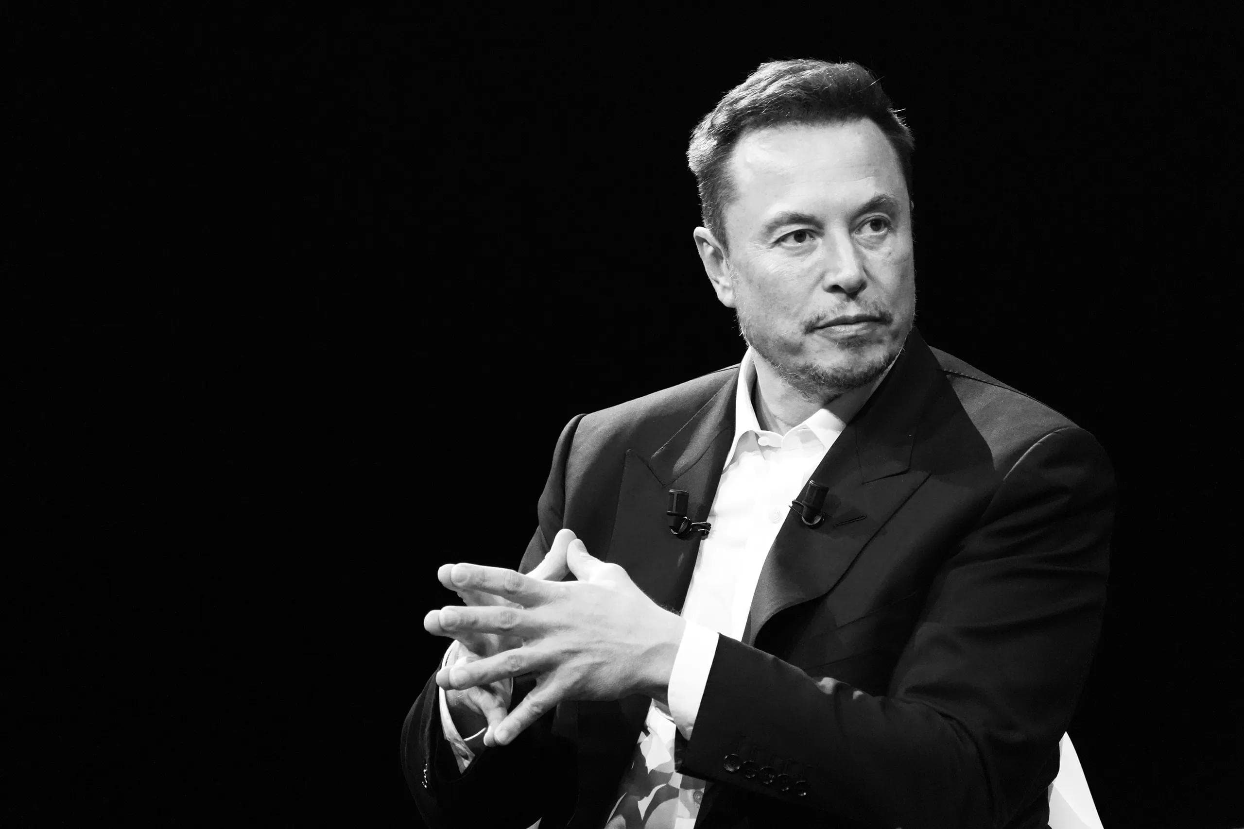 Elon Musk i svart-hvitt på en scene med hendene foldet
