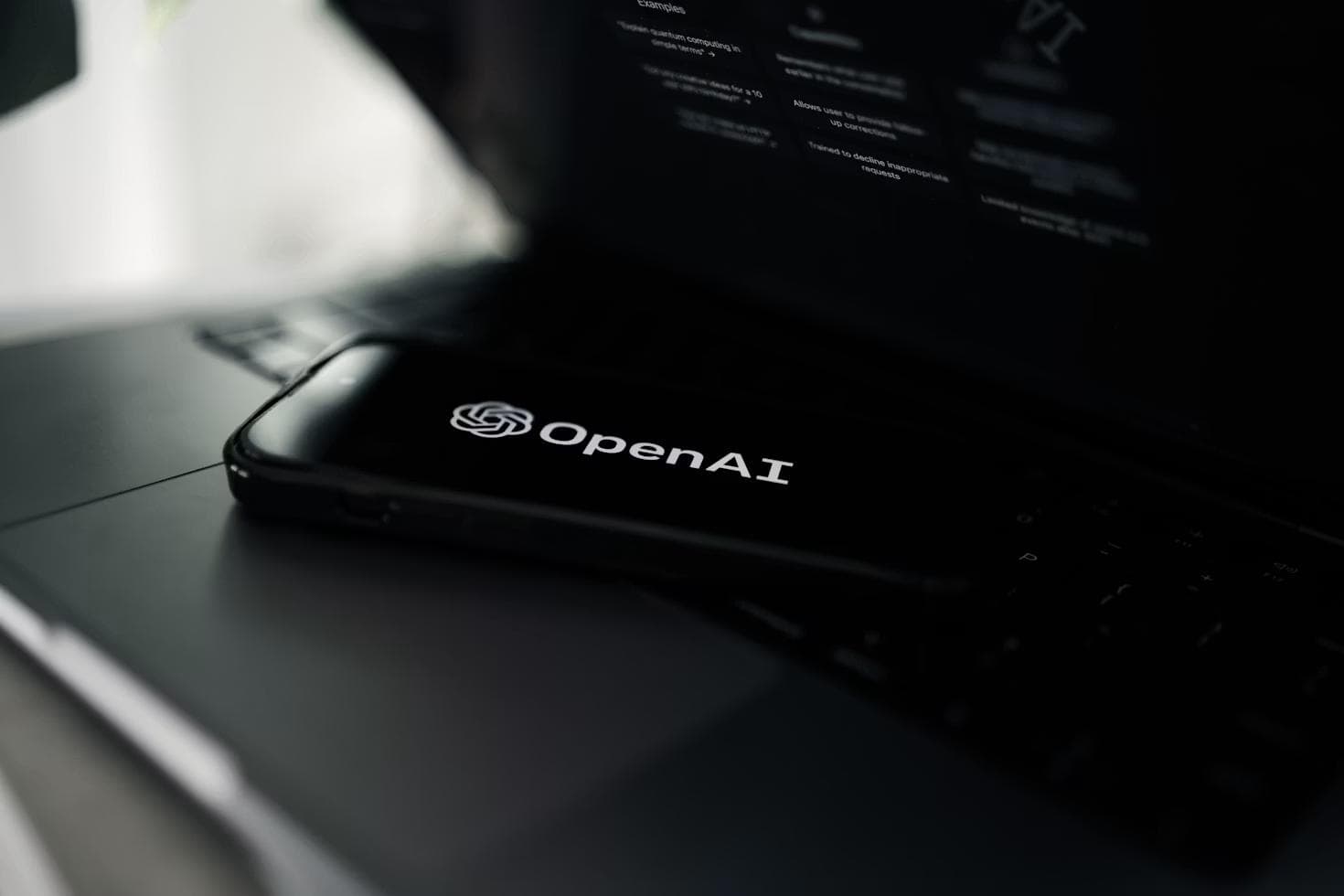 Mobiltelefon med OpenAI-logoen på et mørkt skrivebord